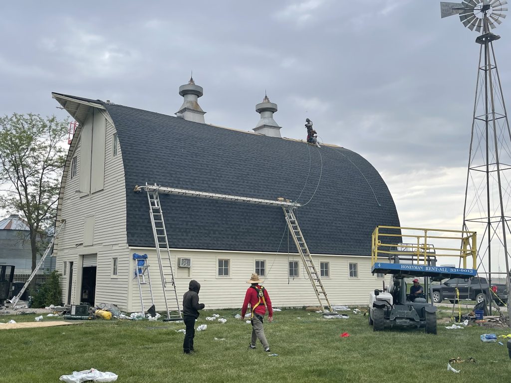 Wide view of a steep barn roof project with crew and ladders.