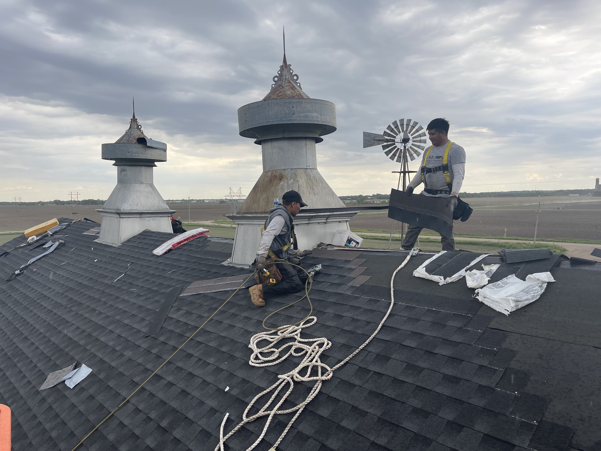 Roofing crew installing shingles on a steep barn roof.