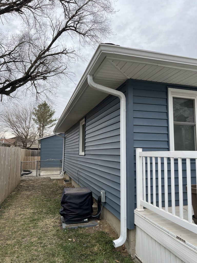 Finished blue siding with white gutter downspout on a residential home.