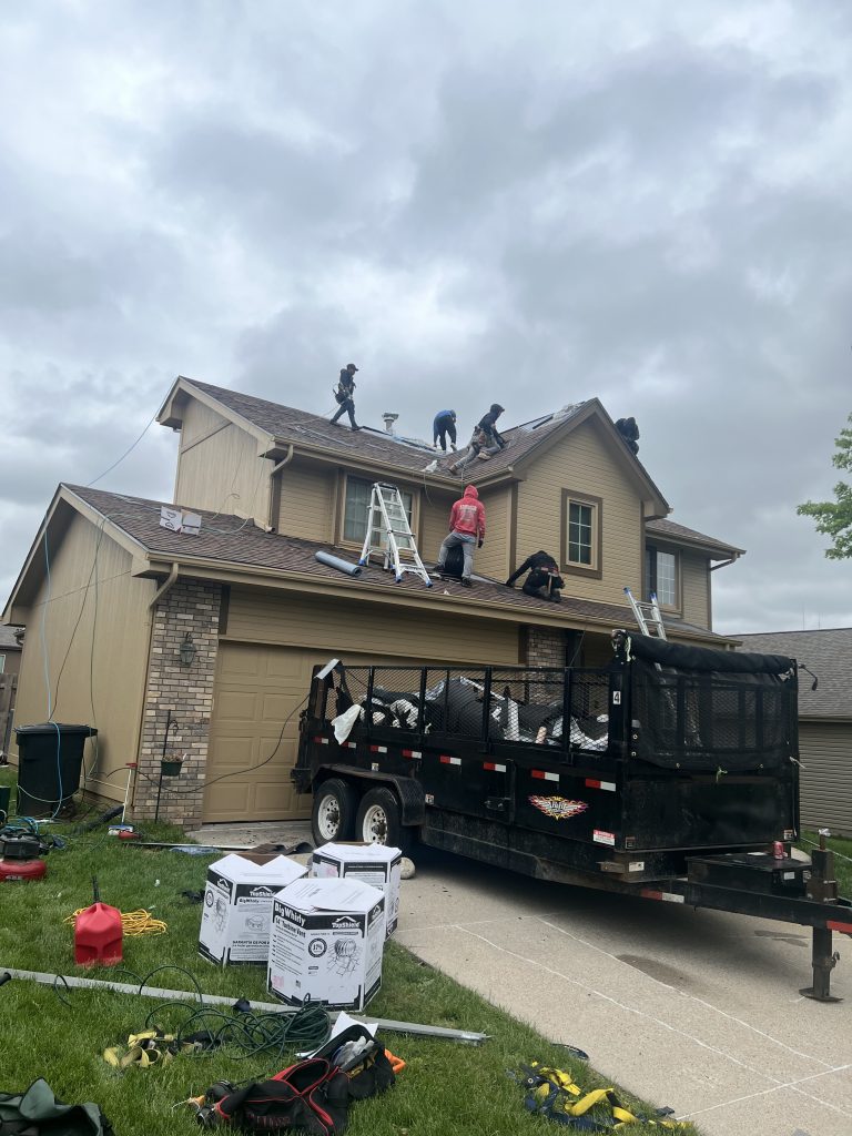 Roof replacement jobsite with crew, materials, and cleanup trailer.