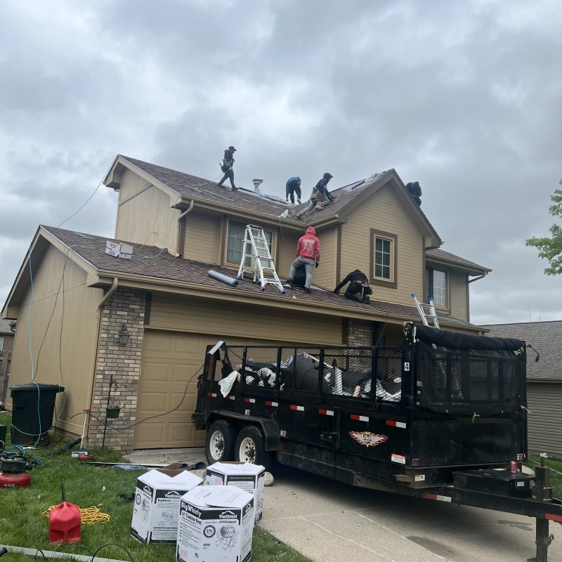 Roof replacement jobsite with crew, materials, and cleanup trailer.