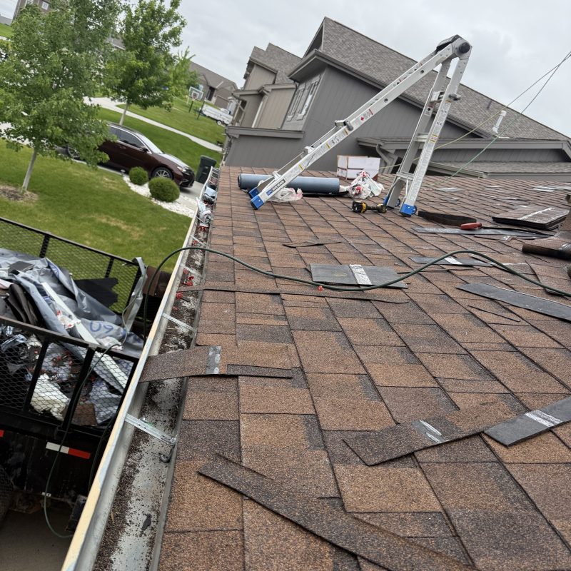 Roof surface during replacement with old shingles and work materials visible.