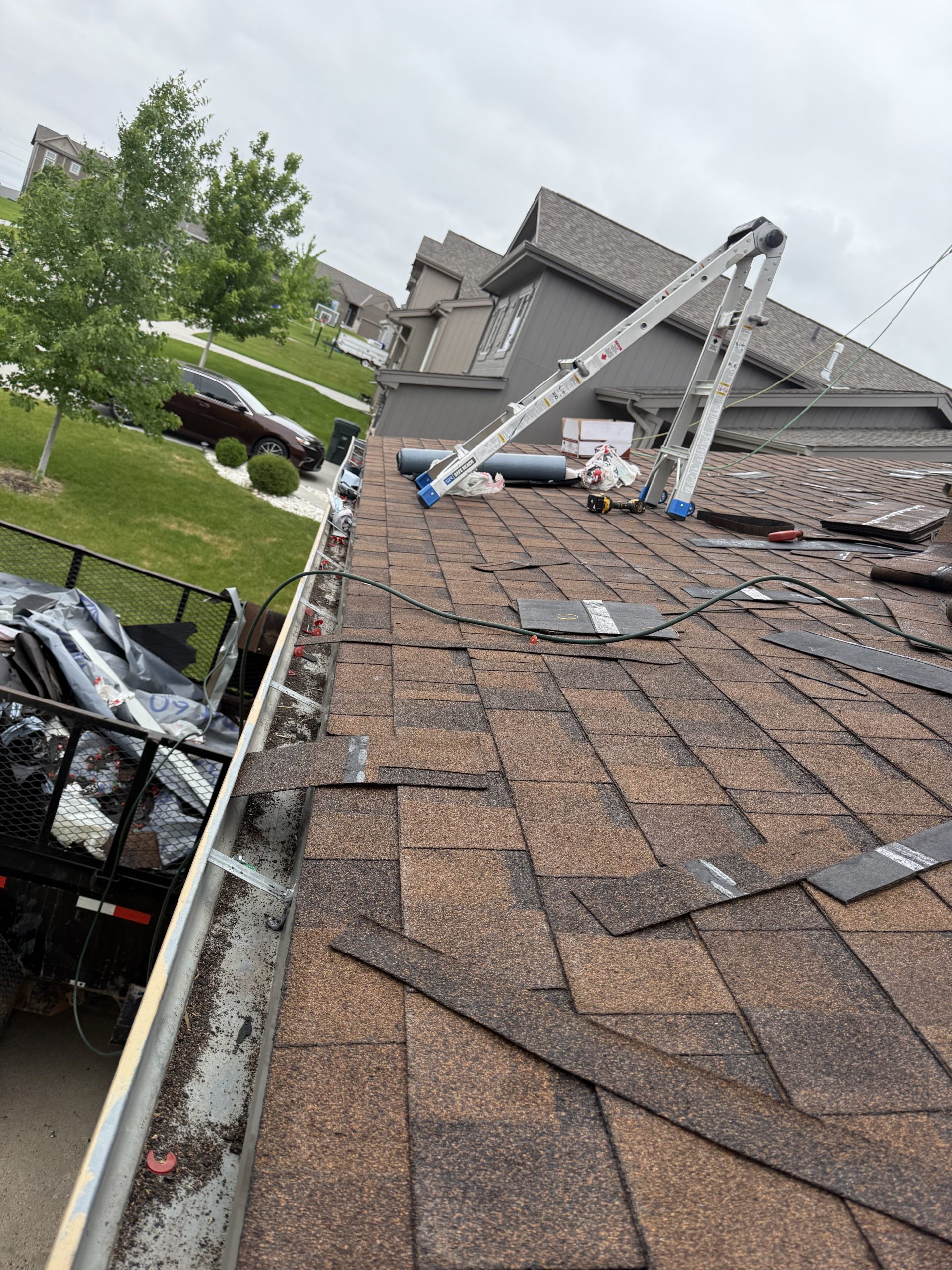 Roof surface during replacement with old shingles and work materials visible.